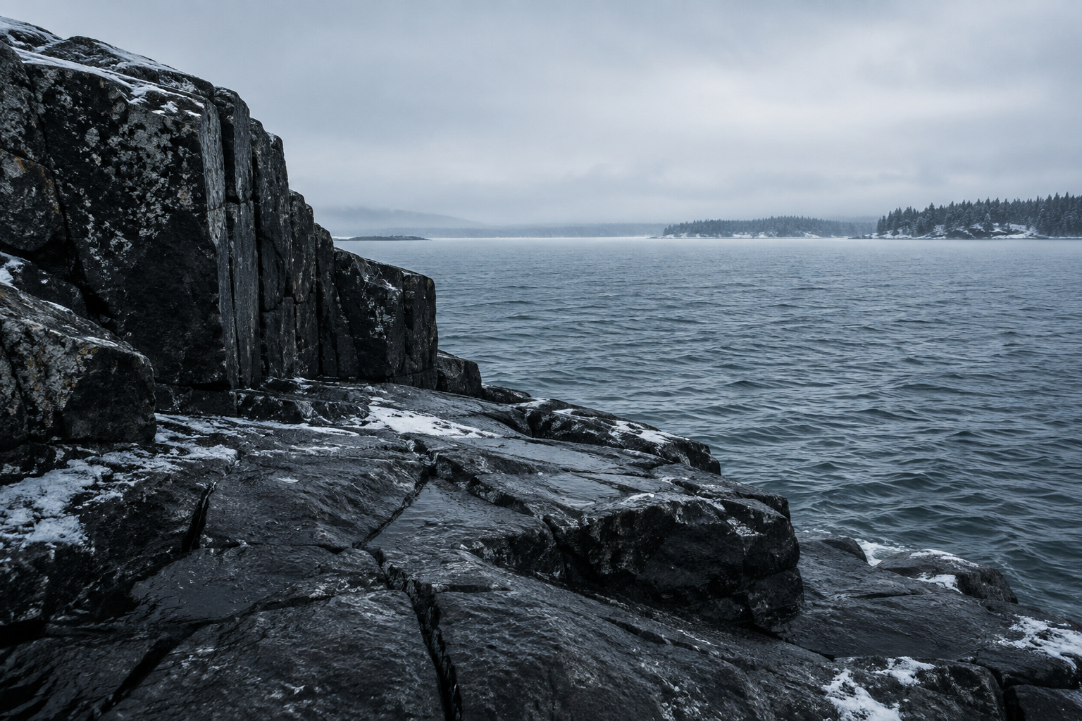 Dark stone at the edge of a cold northern lake, beneath a pale winter sky